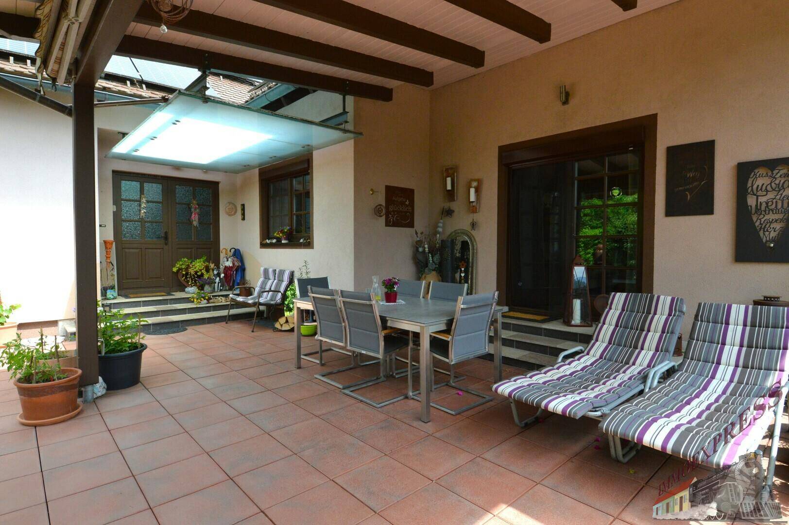 Geräumige, überdachte Terrasse mit Essbereich und Liegestühlen für entspannte Stunden im Freien.