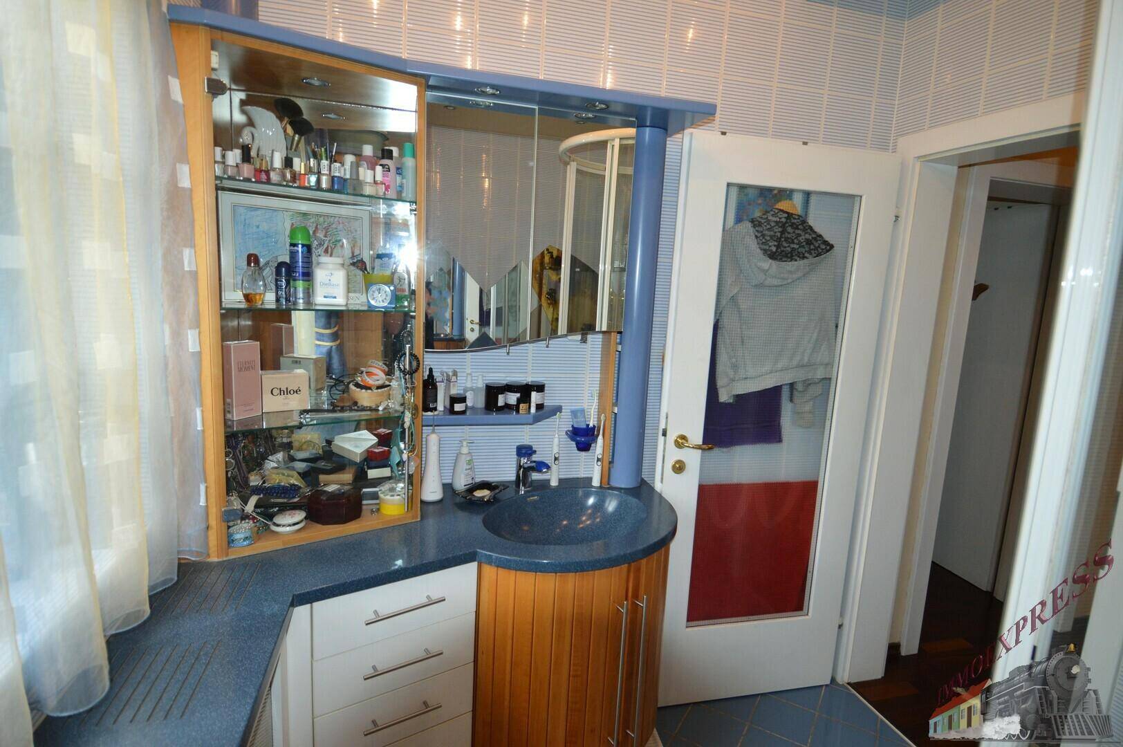 Badezimmer mit Waschtisch, Spiegelschrank und blauen sowie holzfarbenen Schränken.