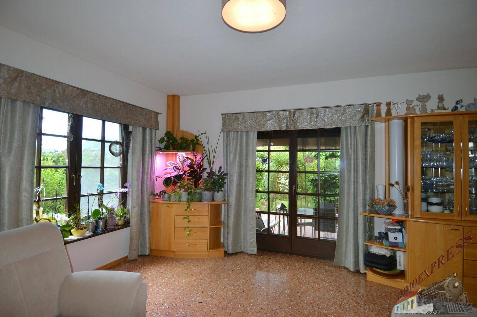 Wohnzimmer mit Terrazzoboden, großen Fenstern und direktem Zugang zur Terrasse oder zum Garten.