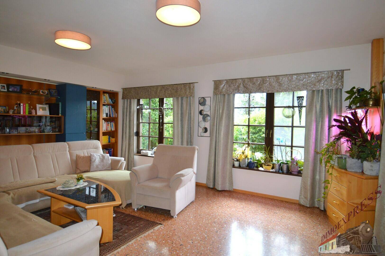 Helles Wohnzimmer mit beigem Sofa, Terrazzoboden und großen Fenstern zum Garten.