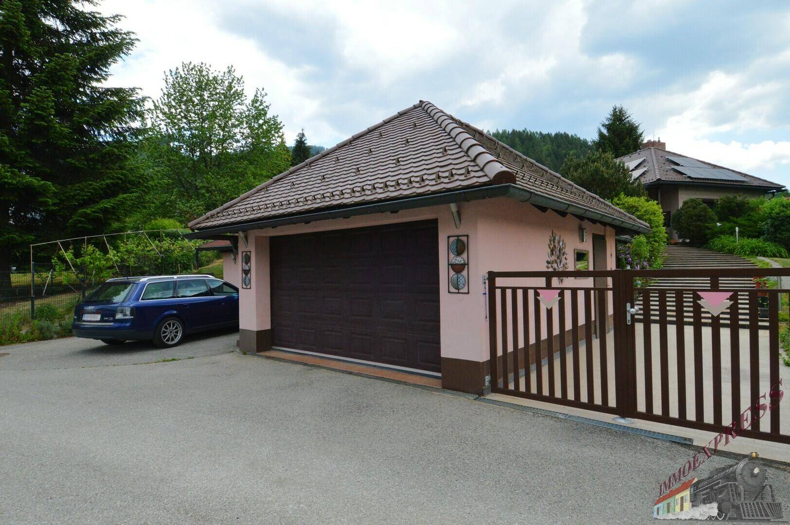 Garage mit dunkelbraunem Tor, davor geparktem Auto und einem Eingangstor.