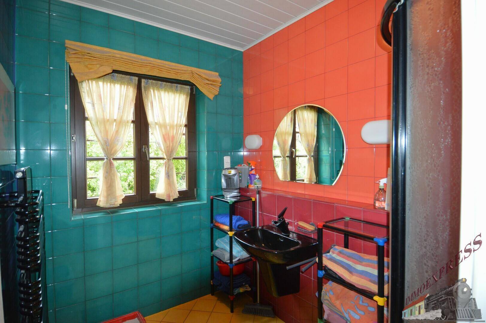 Badezimmer mit farbigen Fliesen, Duschkabine, Waschbecken und Fenster für Tageslicht.