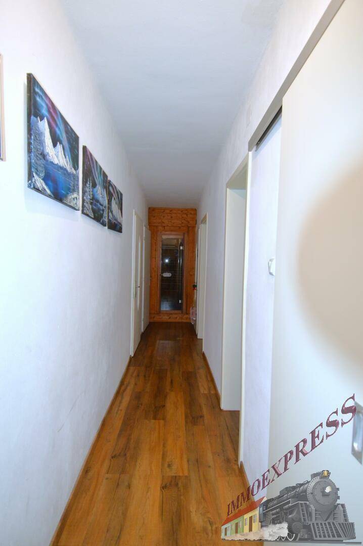 Langer, heller Flur mit Holzboden und dekorativen Bildern an der Wand.