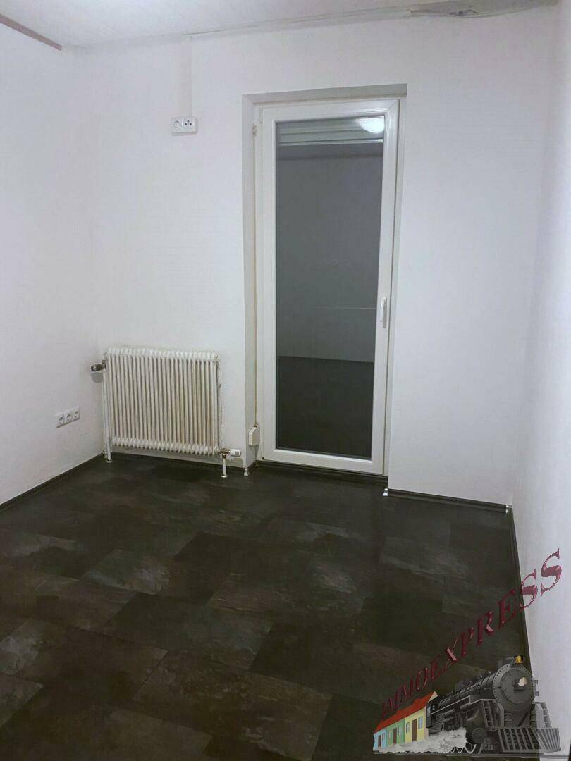 Leerer Raum mit weißen Wänden, dunklem Boden und Zugang nach draußen, inklusive Heizkörper.