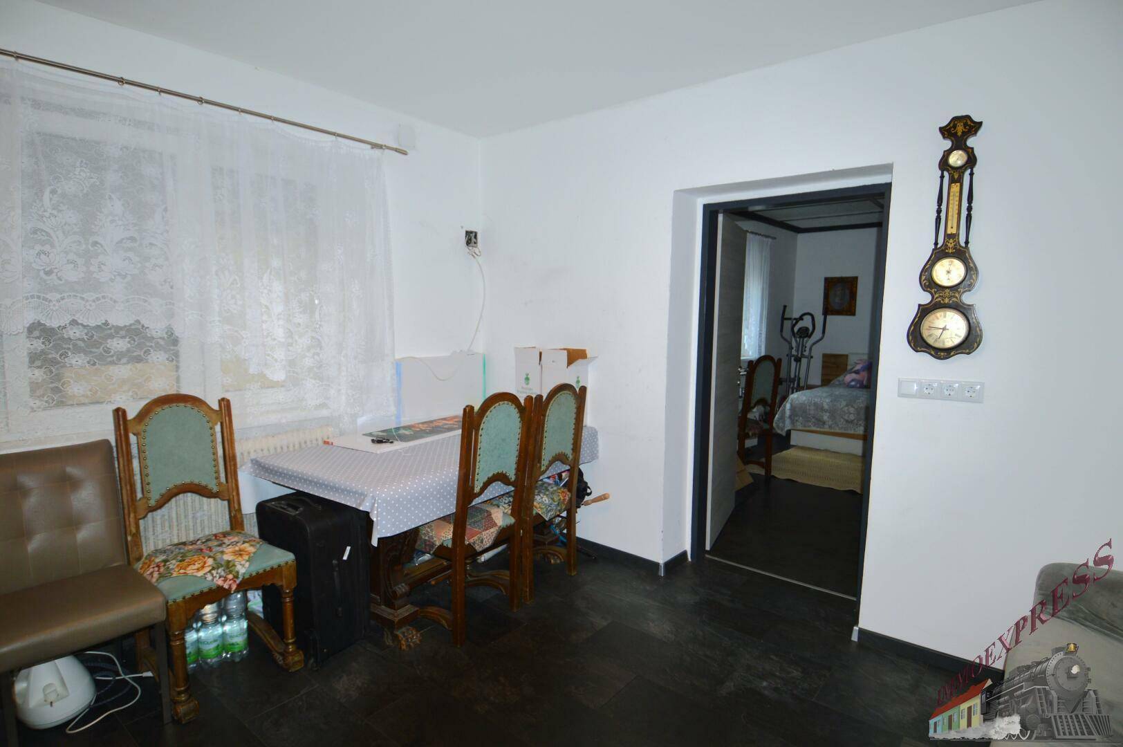 Essbereich mit Tisch und Stühlen, angrenzend an ein Schlafzimmer, mit traditioneller Wanduhr.