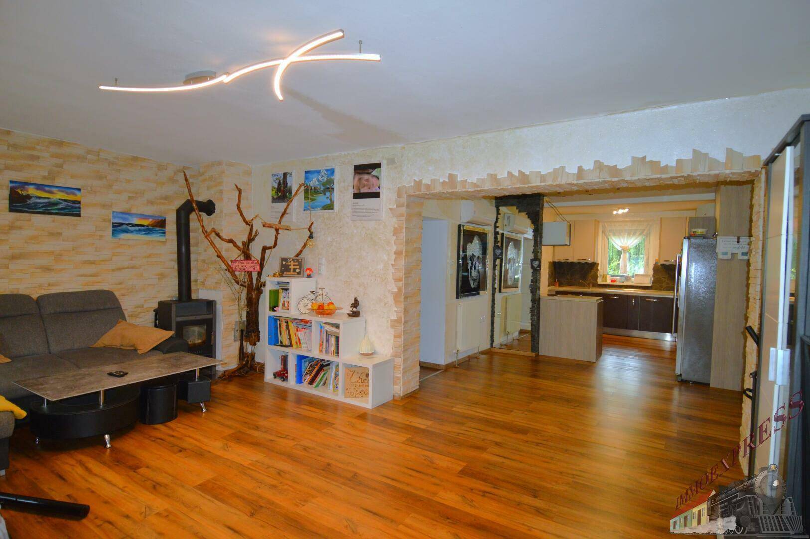 Geräumiges Wohnzimmer mit Holzboden, Kaminofen und offener Verbindung zur Küche.