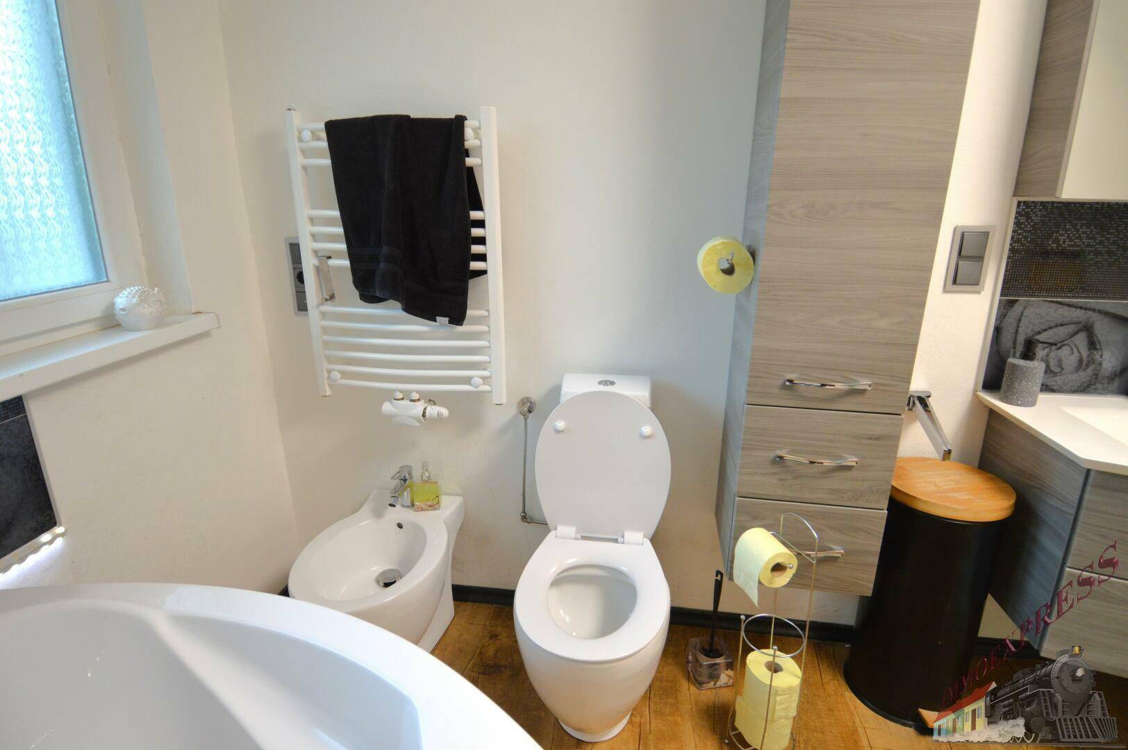 Badezimmer mit Toilette, Bidet und Handtuchheizkörper, neben einer Badewanne.
