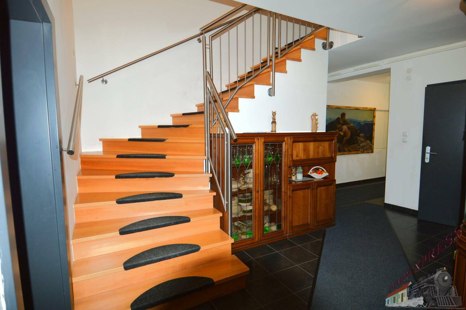Heller Eingangsbereich mit Holztreppe, Edelstahlgeländer und einem dekorativen Holzschrank.