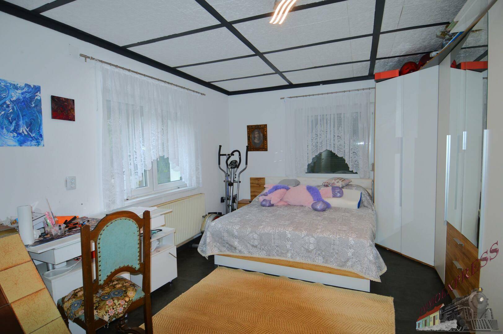 Schlafzimmer mit Doppelbett, Kleiderschrank, Trainingsgerät und dunklem Bodenbelag.