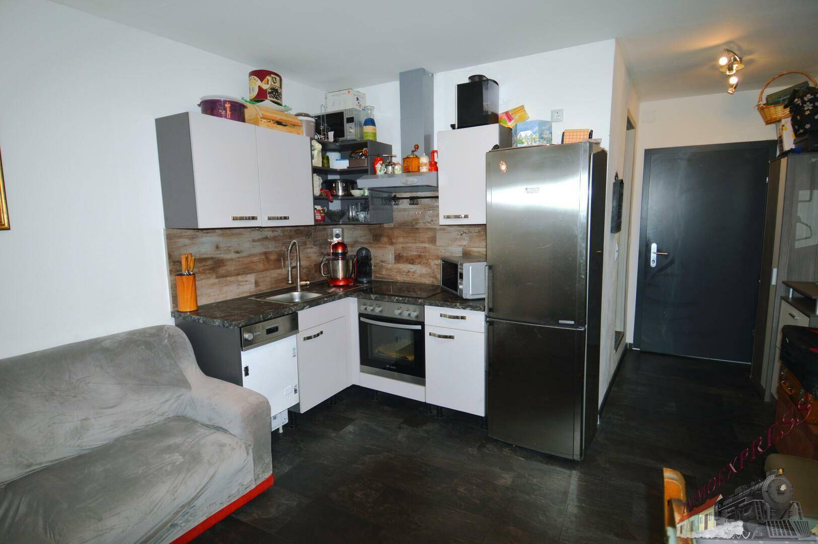 Kleine, funktionale Küche mit weißen Schränken, Holzoptik-Rückwand und integrierten Geräten.