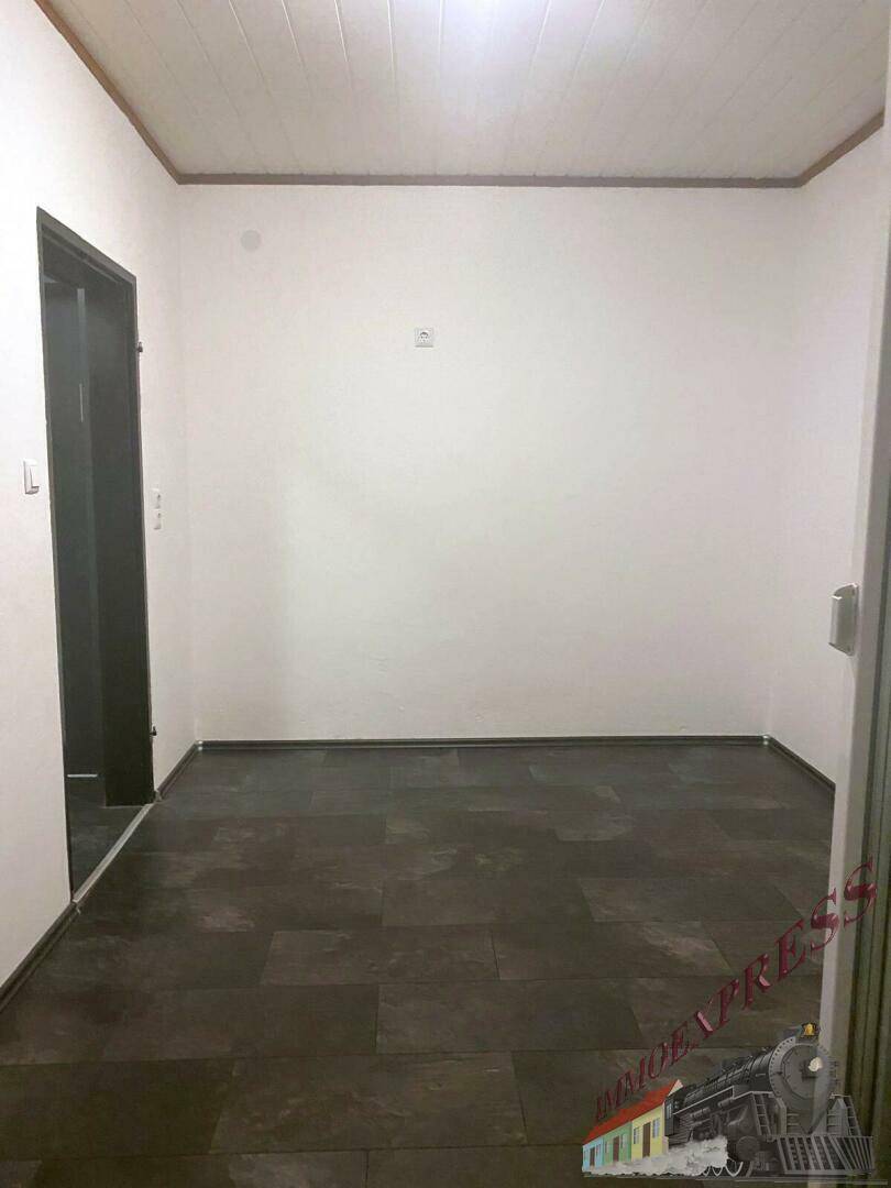 Leerer, unmöblierter Raum mit dunklem Boden und weiß gestrichenen Wänden.