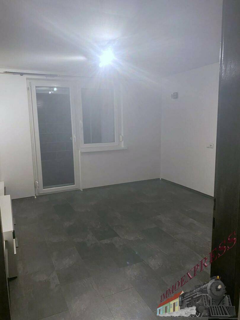 Heller, unmöblierter Raum mit dunklem Boden und Fenster mit Zugang nach draußen.