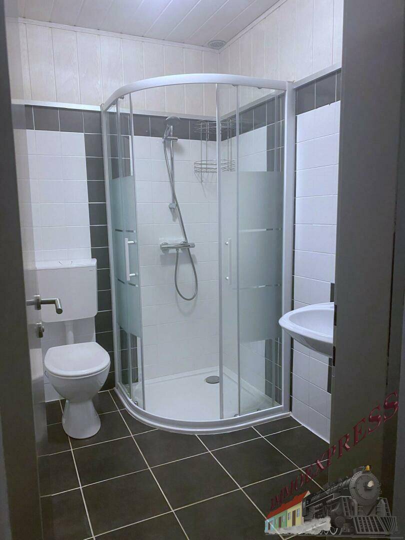 Modernes Badezimmer mit Duschkabine, WC, Waschbecken und dunklen Bodenfliesen.