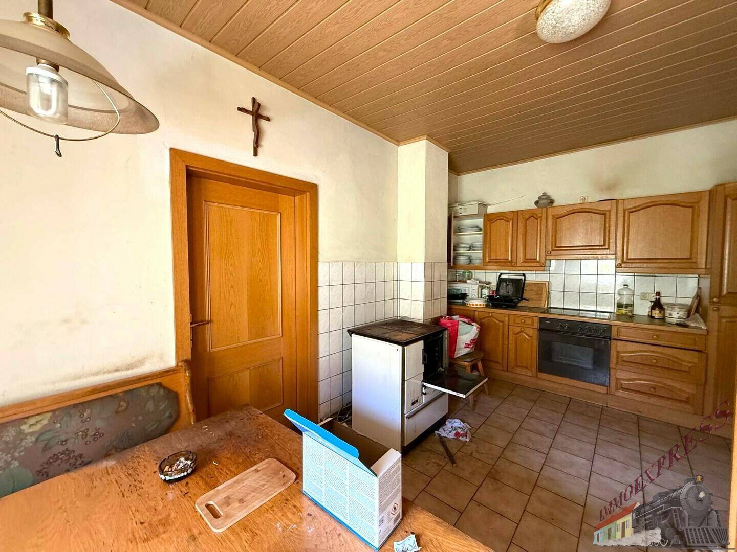 Traditionelle Küche mit Holzschränken, Fliesenboden, einem Holzofen und einem Esstisch mit Eckbank.