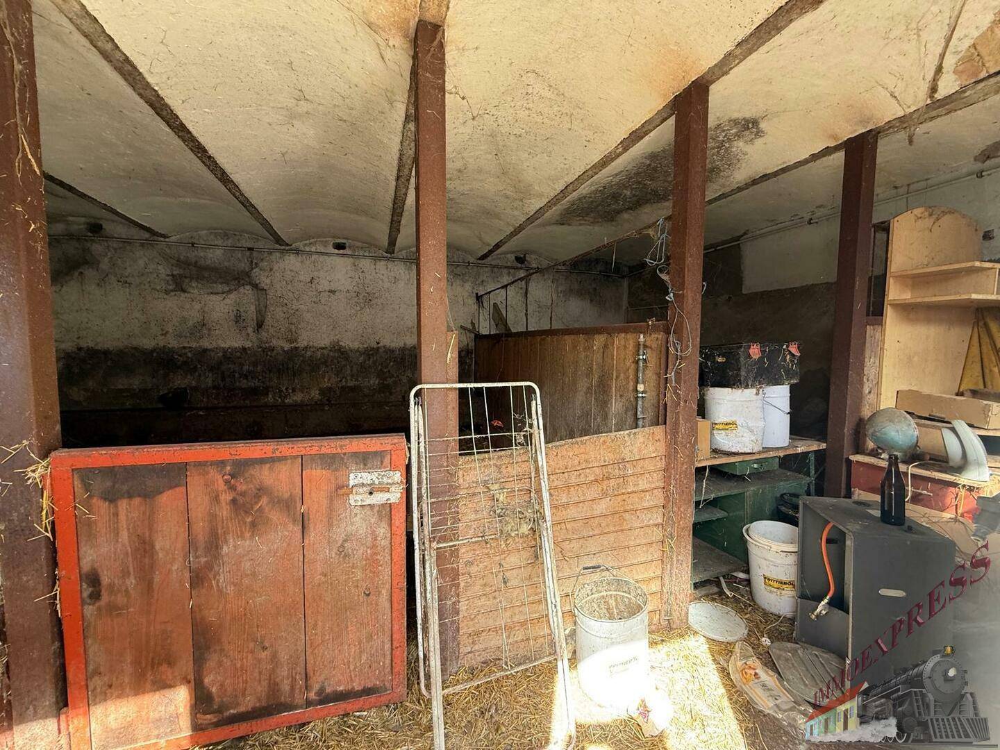 Rustikaler Innenraum eines alten Stallgebäudes mit Holzbalken und Lagerflächen.