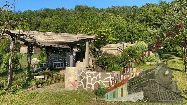 Gartenbereich mit Holzpergola, Steinmauern und Treppen, umgeben von üppiger Vegetation.