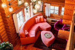 Gemütliches Wohnzimmer mit großer orangeroter Couch, passendem Hocker und Holzwänden.