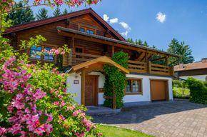 Eingangsbereich des Hauses mit Garage, umgeben von blühenden rosa Sträuchern unter blauem Himmel.