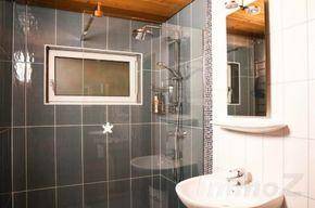 Modernes Badezimmer mit grauen Fliesen, Duschkabine und kleinem Fenster für Tageslicht.