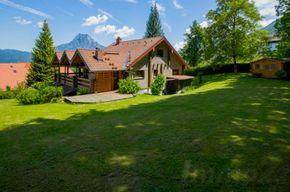 Charmantes Haus mit großem Rasen und beeindruckendem Bergblick unter blauem Himmel.