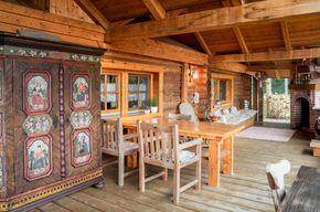 Gemütliche Holzloggia mit Esstisch, Stühlen und einem traditionellen bemalten Schrank.