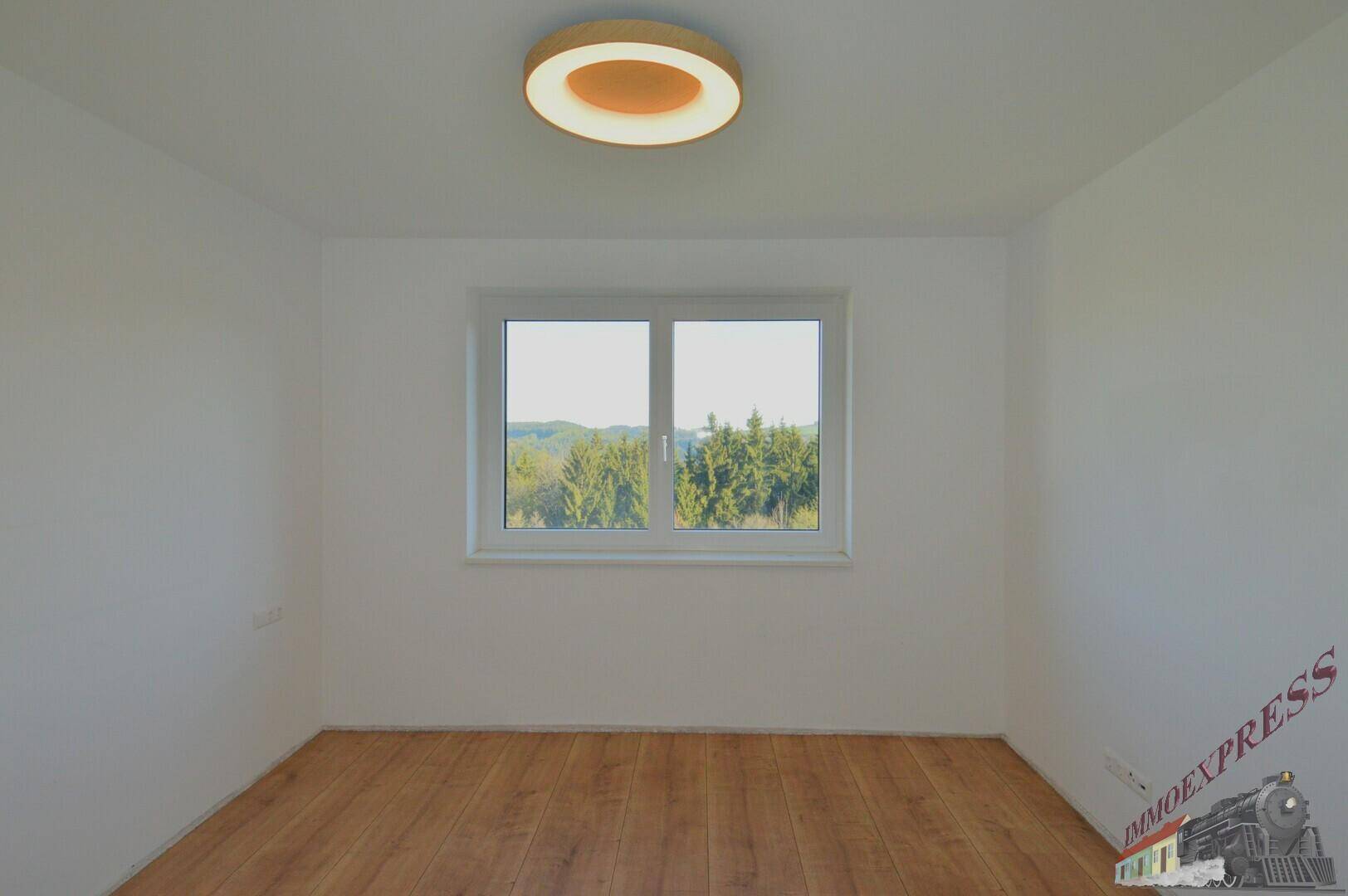 Heller, leerer Raum mit Holzboden und Ausblick auf die umliegende Natur.