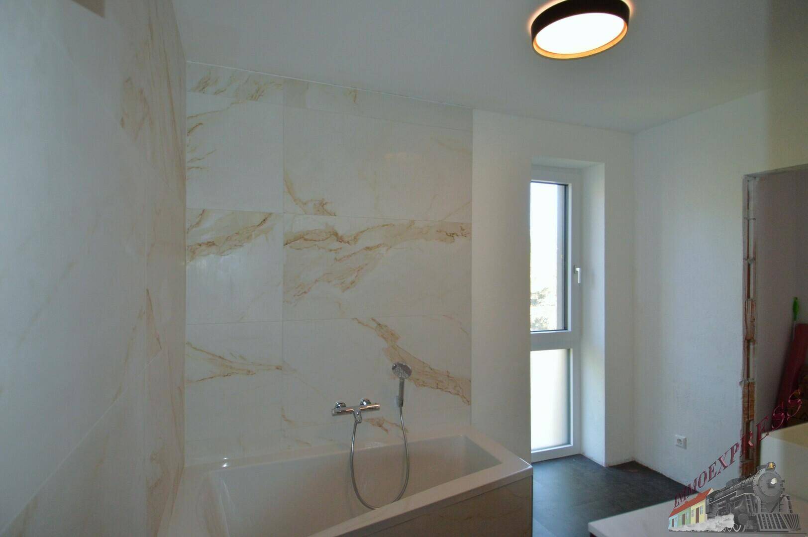 Helles Badezimmer mit Badewanne, Marmorfliesen und einem Fenster für Tageslicht.