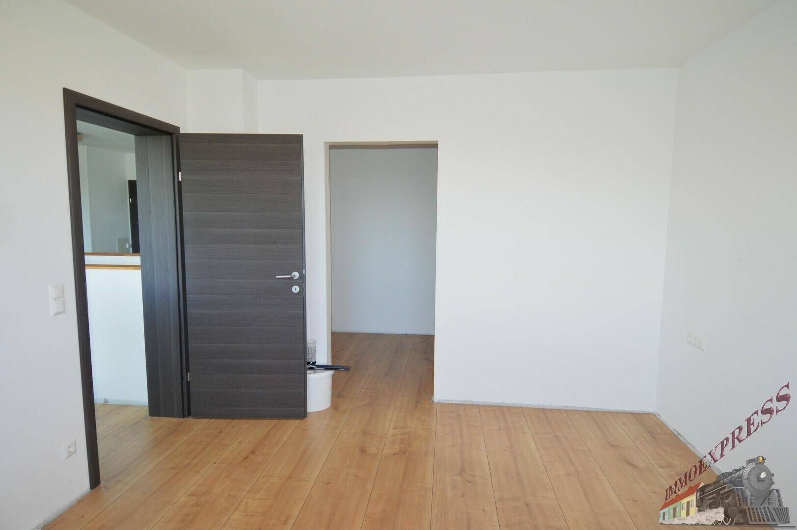 Leerer Raum mit Holzboden und modernen dunklen Türen, der verschiedene Bereiche verbindet.