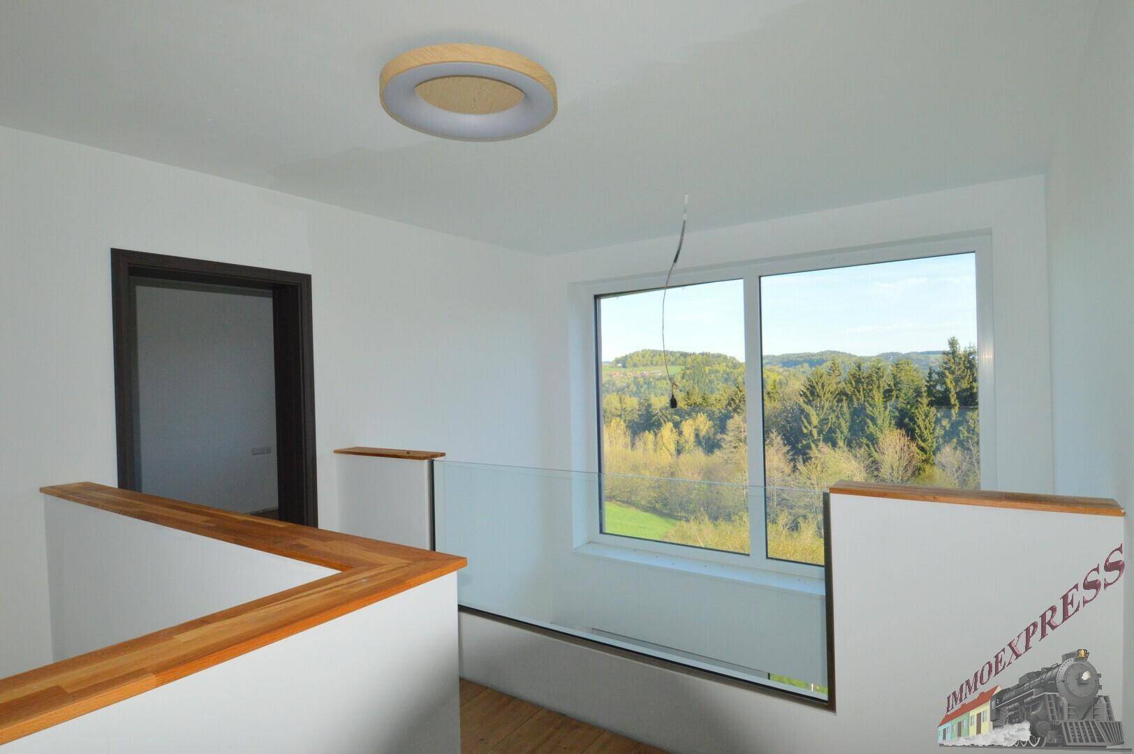 Heller Flurbereich mit Glasgeländer und weitem Blick ins Grüne durch das große Fenster.