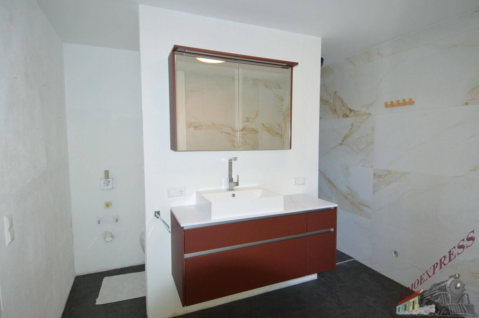 Modernes Badezimmer mit Waschtisch, Spiegelschrank und stilvollen Marmorfliesen an der Wand.