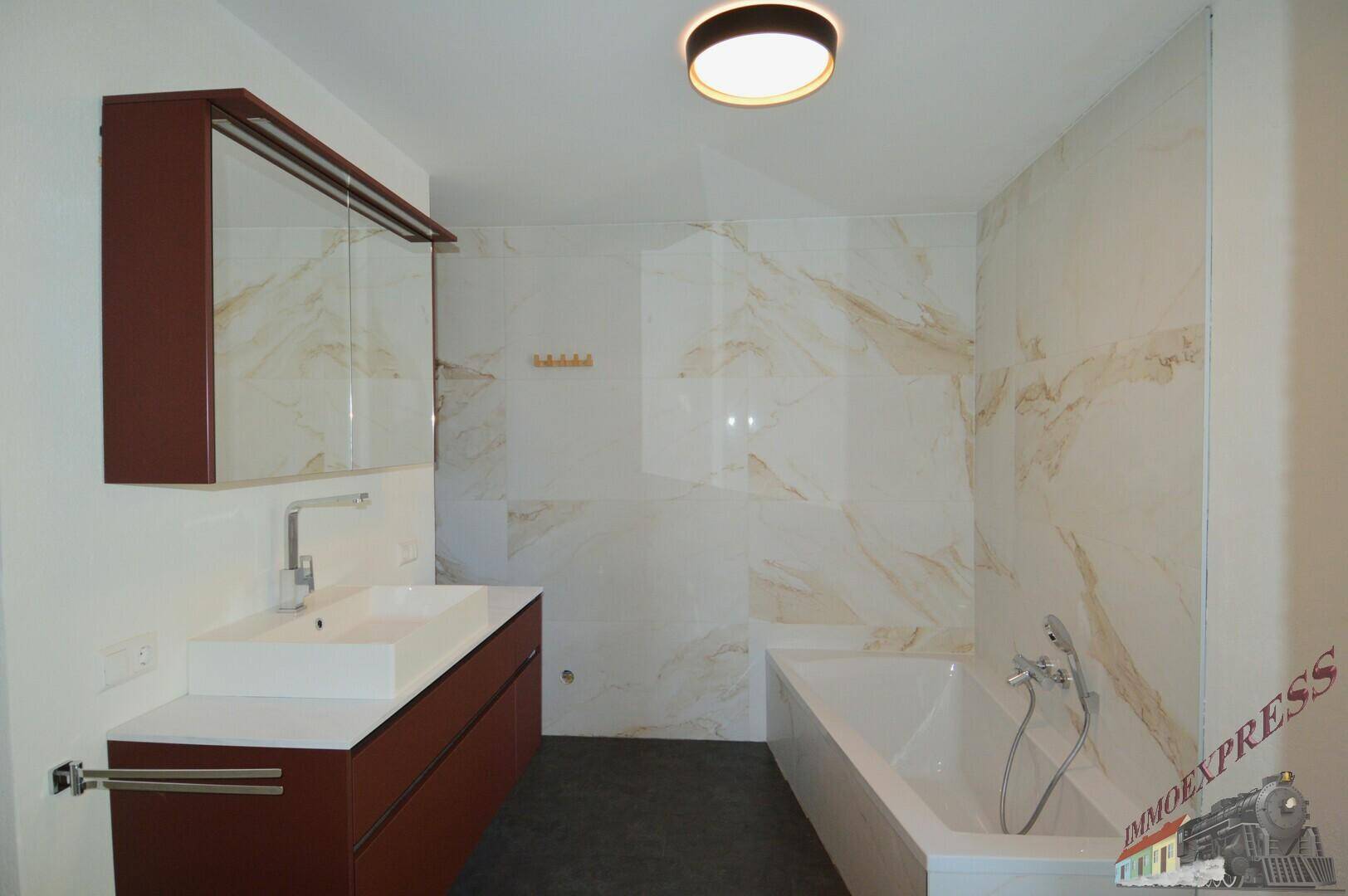 Modernes Badezimmer mit Badewanne, Einzelwaschbecken und eleganten Marmorfliesen an der Wand.
