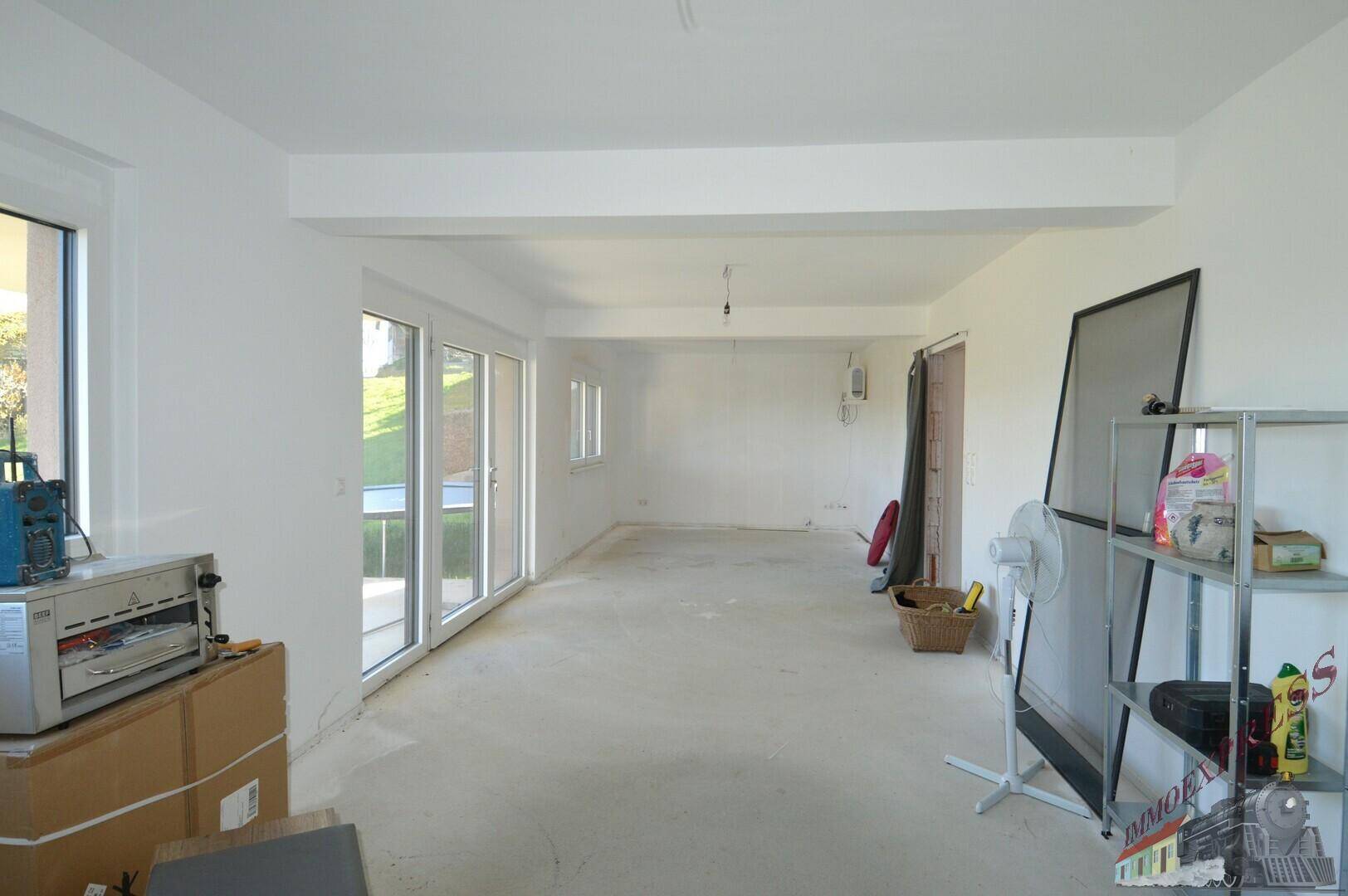 Großer, heller Raum im Rohbau mit mehreren Fenstern und Terrassenzugang.