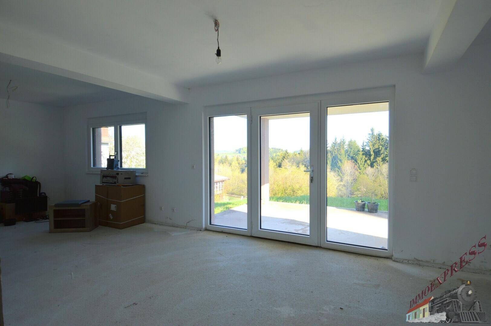 Geräumiger Wohnbereich im Rohbau mit großen Glasfronten und Zugang zur Terrasse.