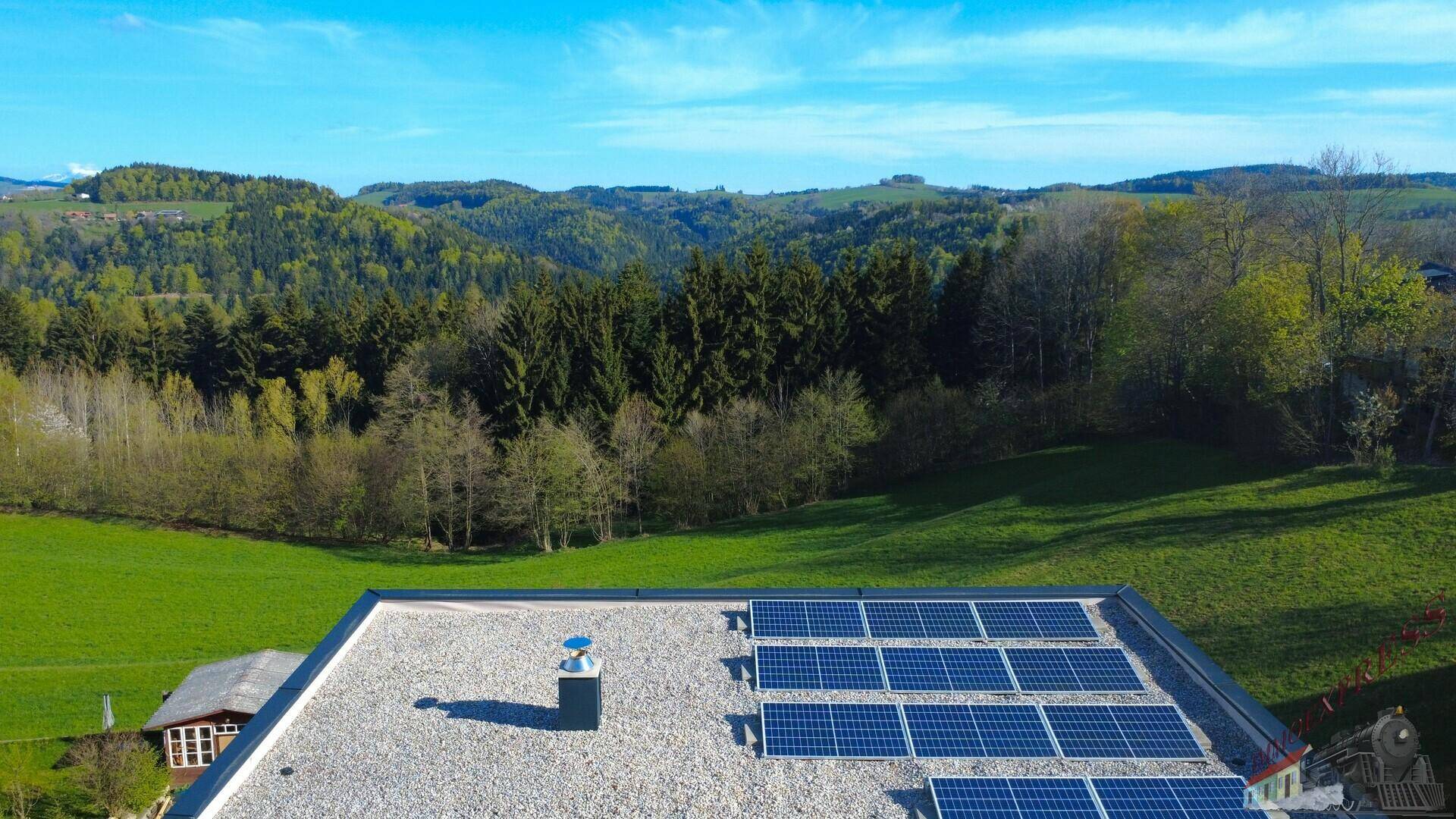 Flachdach eines Neubaus mit Photovoltaikanlage und weitem Blick ins Grüne.