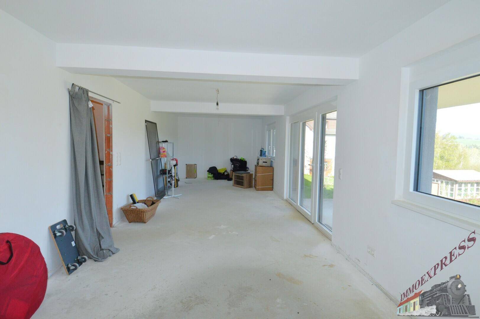Weitläufiger Raum im Rohbau mit viel Tageslicht und Blick ins Grüne.