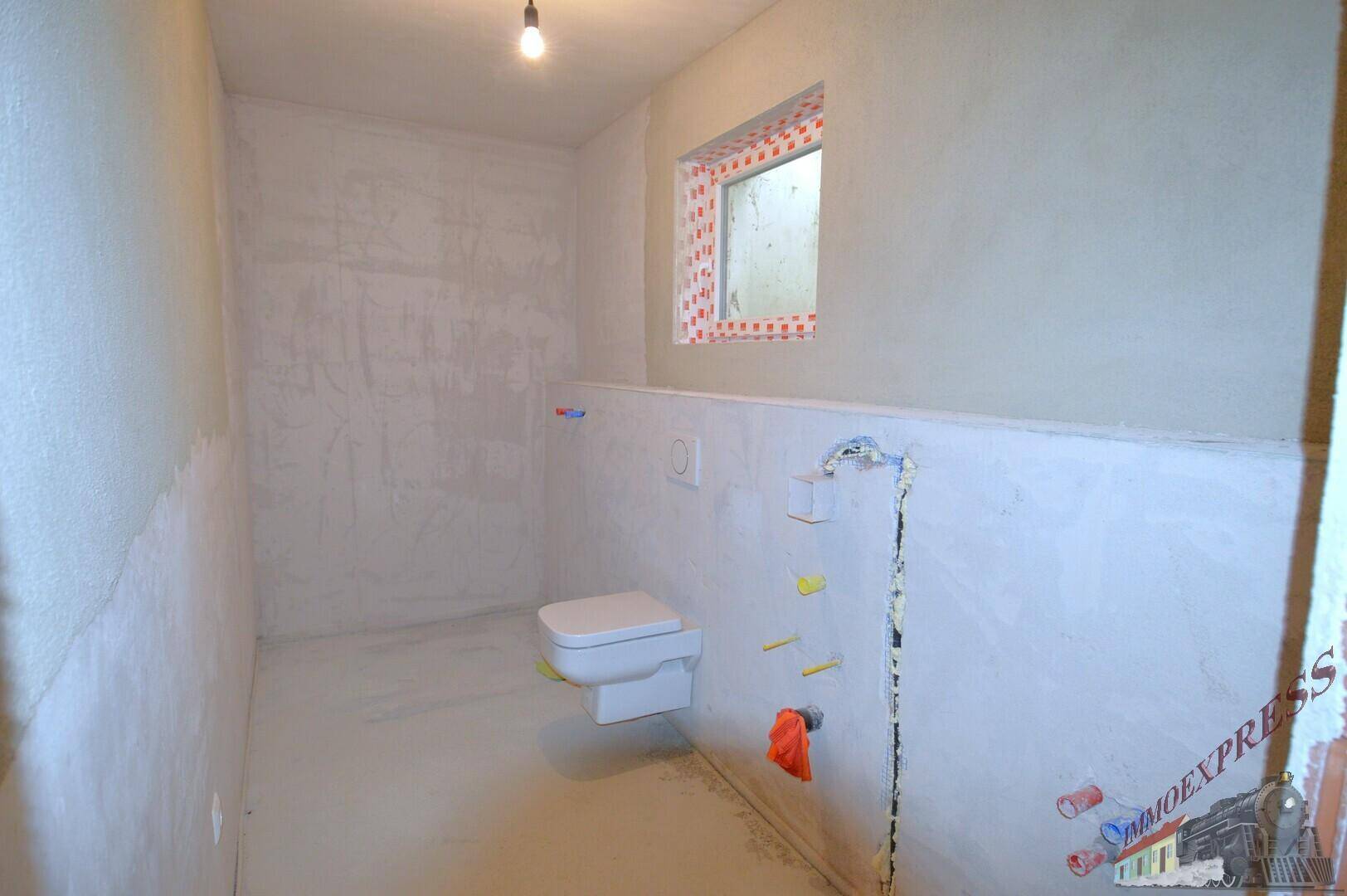 Unfertiges WC mit wandhängender Toilette und kleinem Fenster für Belüftung.