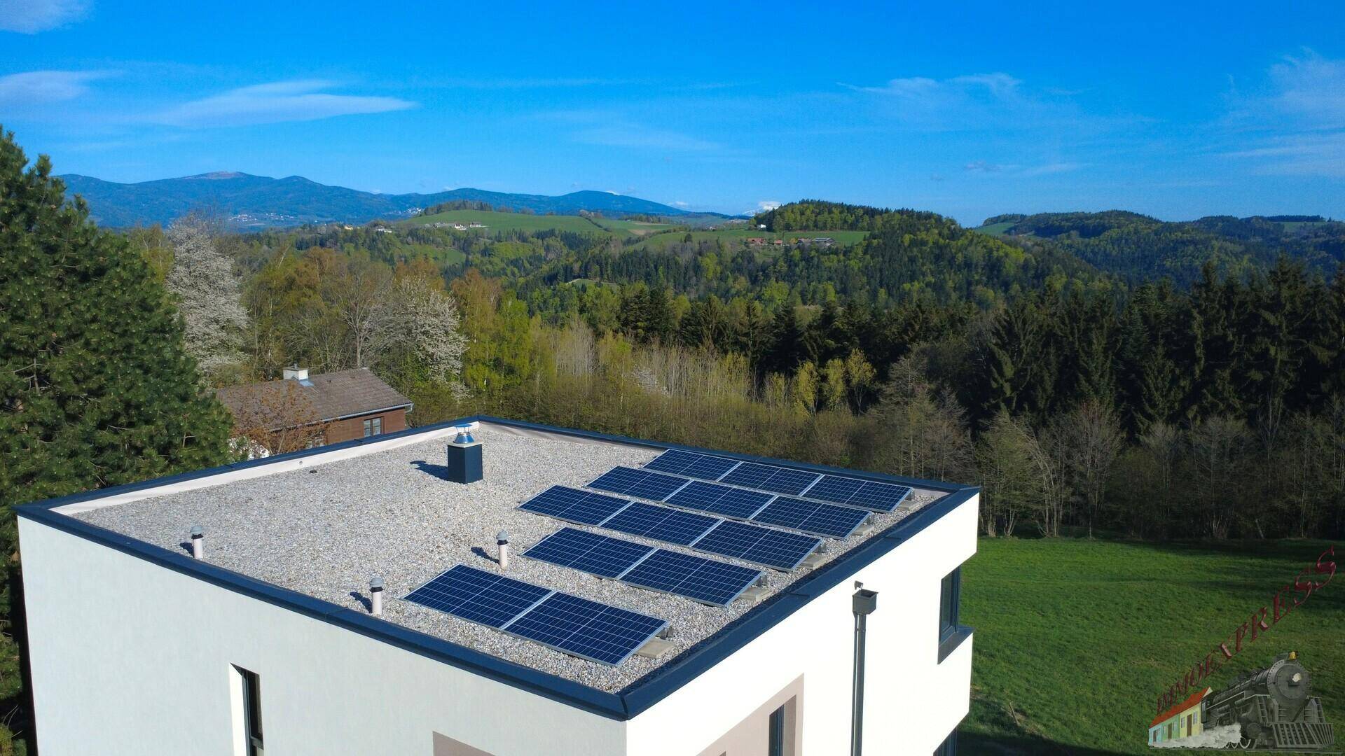 Flachdach eines modernen Hauses mit installierten Photovoltaik-Modulen und weitem Blick in die Landschaft.