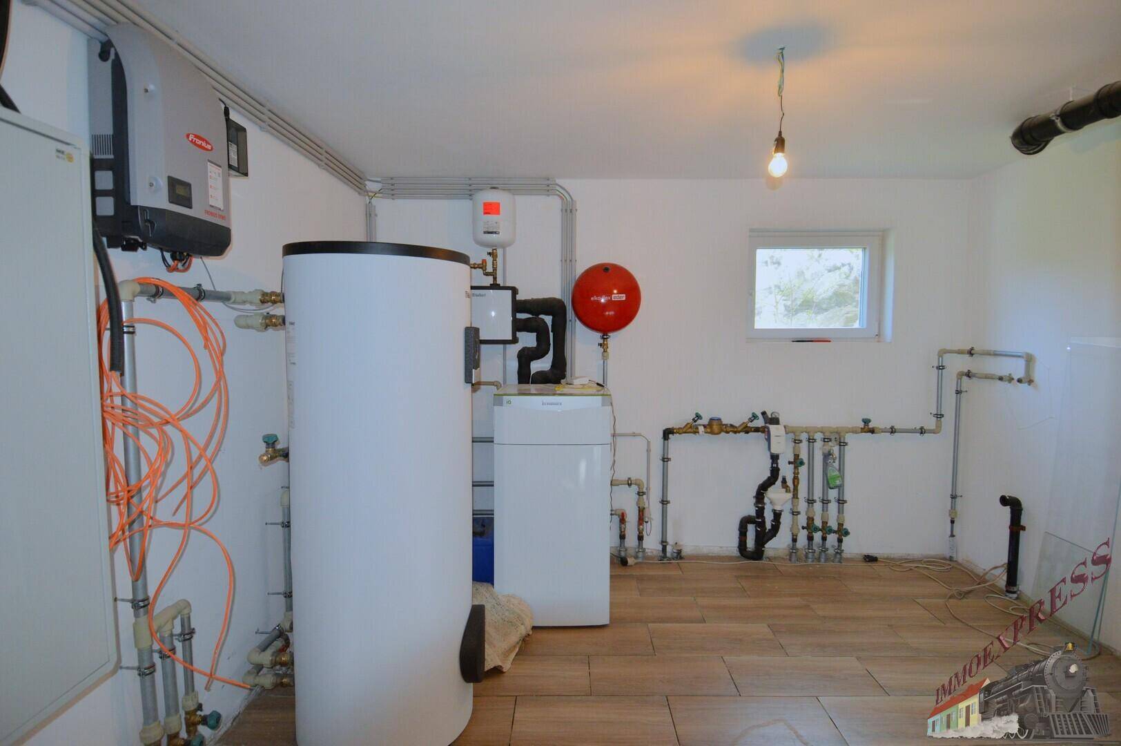 Technikraum im Keller mit Heizungsanlage, Warmwasserspeicher und Fliesenboden.