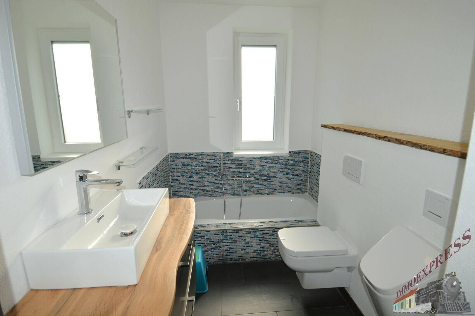 Modernes Badezimmer mit Badewanne, wandhängendem WC und stilvollen Mosaikfliesen.