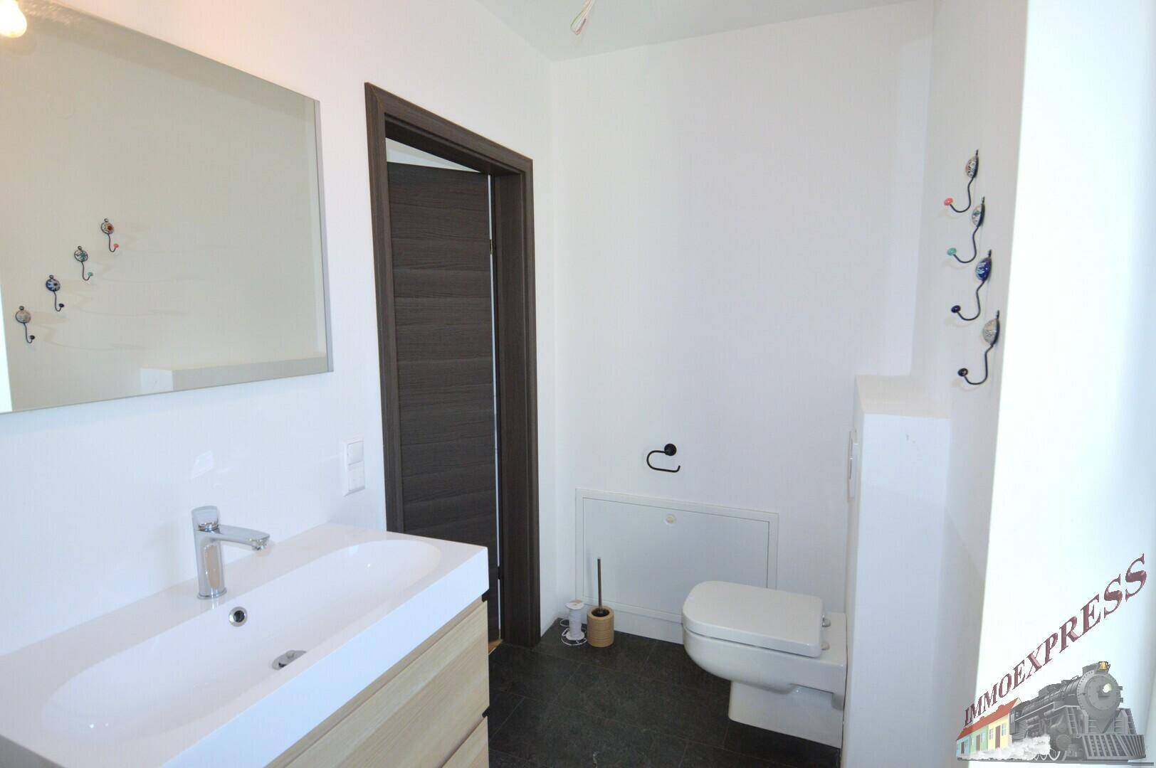 Badezimmer mit modernem Waschtisch, wandhängendem WC und Spiegel, in hellen Farbtönen gehalten.