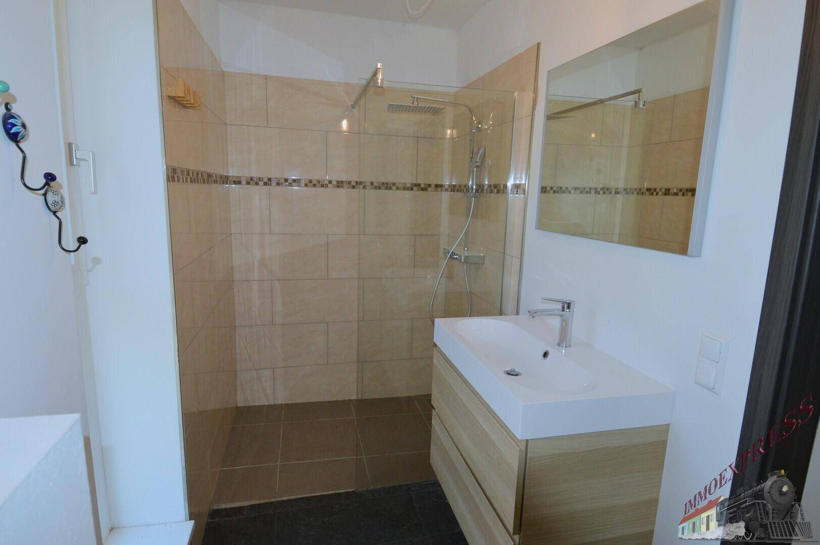 Modernes Badezimmer mit großer begehbarer Dusche, hellem Waschtisch und Spiegel.
