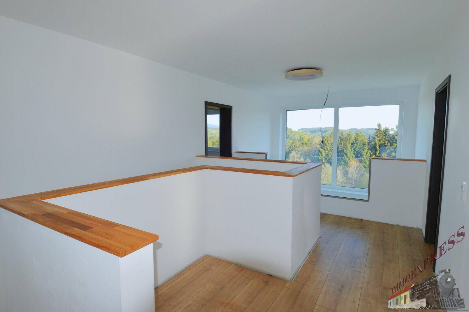 Heller Flur im Obergeschoss mit Holzfußboden und Blick in die grüne Umgebung durch das Fenster.