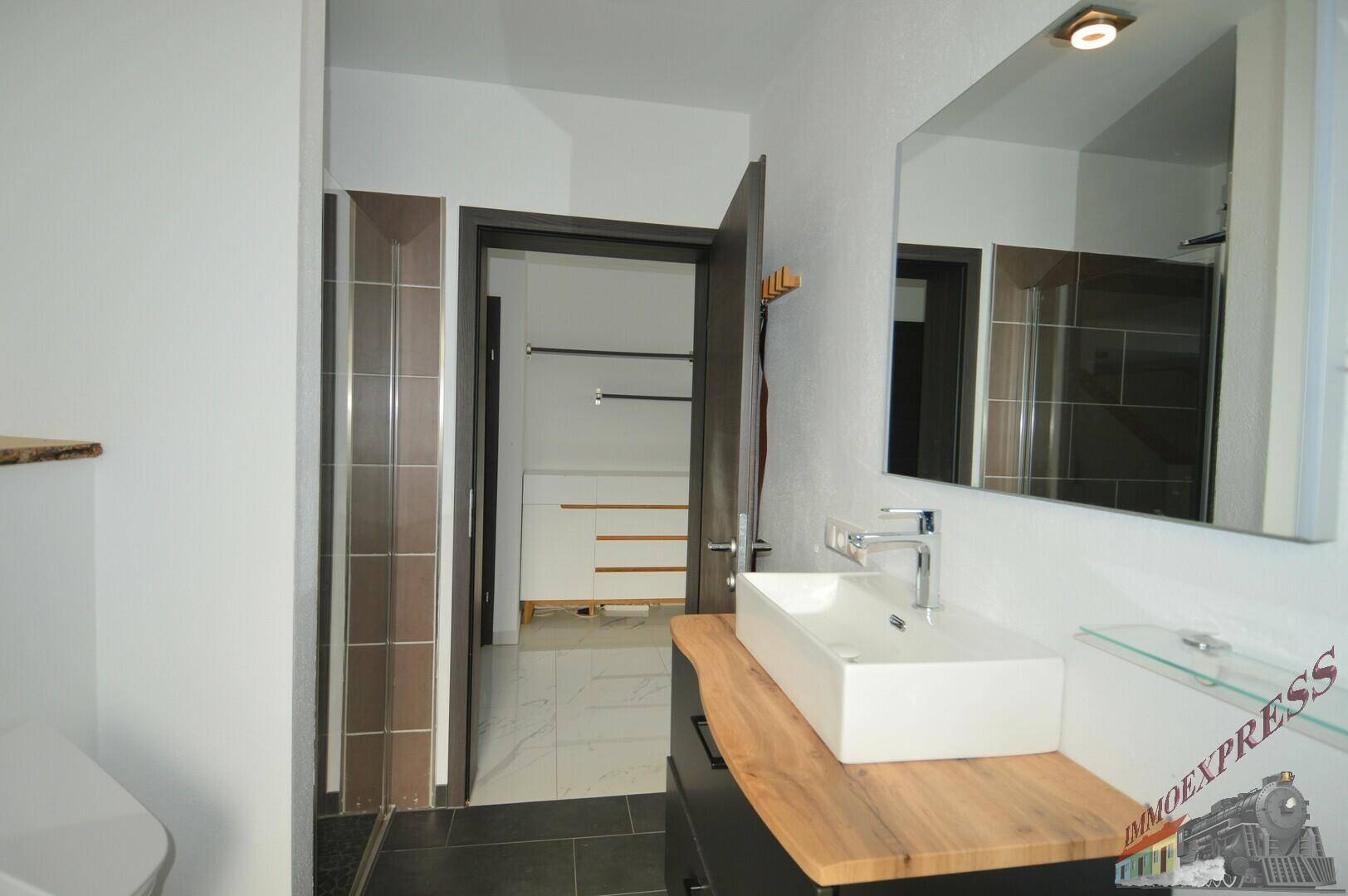 Badezimmer mit modernem Waschtisch und Spiegel, angrenzend an einen begehbaren Kleiderschrank.