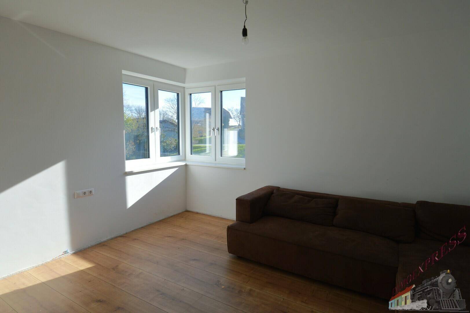 Gemütliches Wohnzimmer mit braunem Sofa und großen Fenstern, die viel Tageslicht hereinlassen.