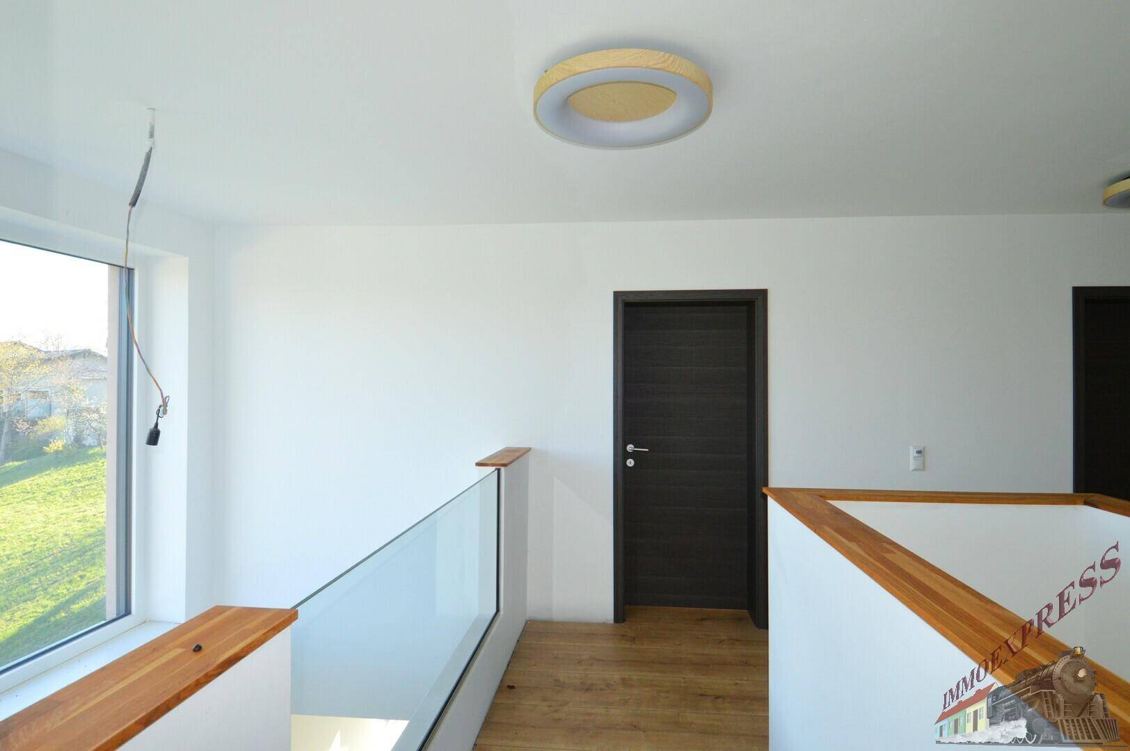 Heller Flur im Obergeschoss mit Holzgeländer und dunklen Türen, die zu den Zimmern führen.