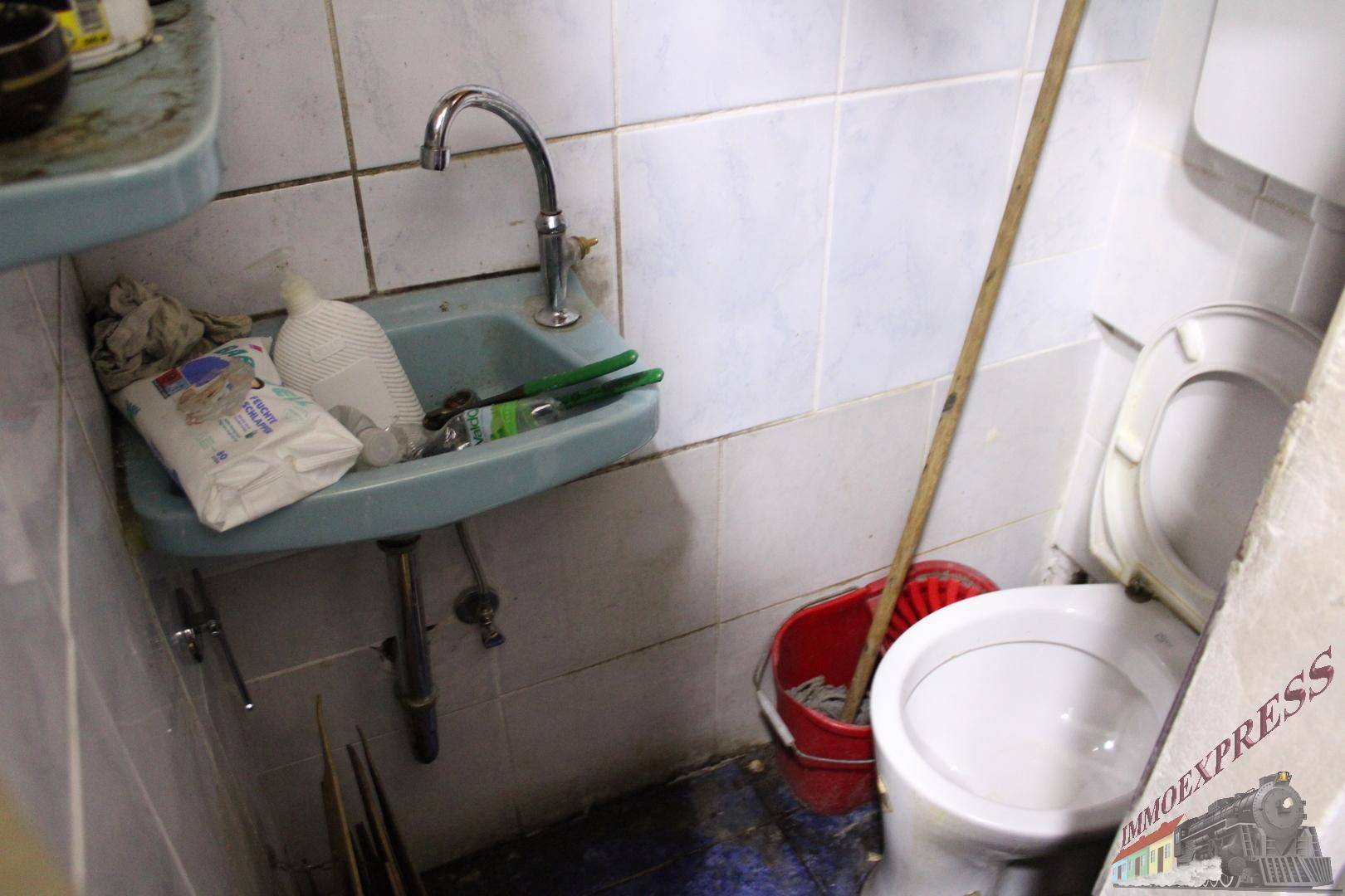 Kleines, einfaches Badezimmer mit Waschbecken, Toilette und Fliesen an den Wänden und auf dem Boden.