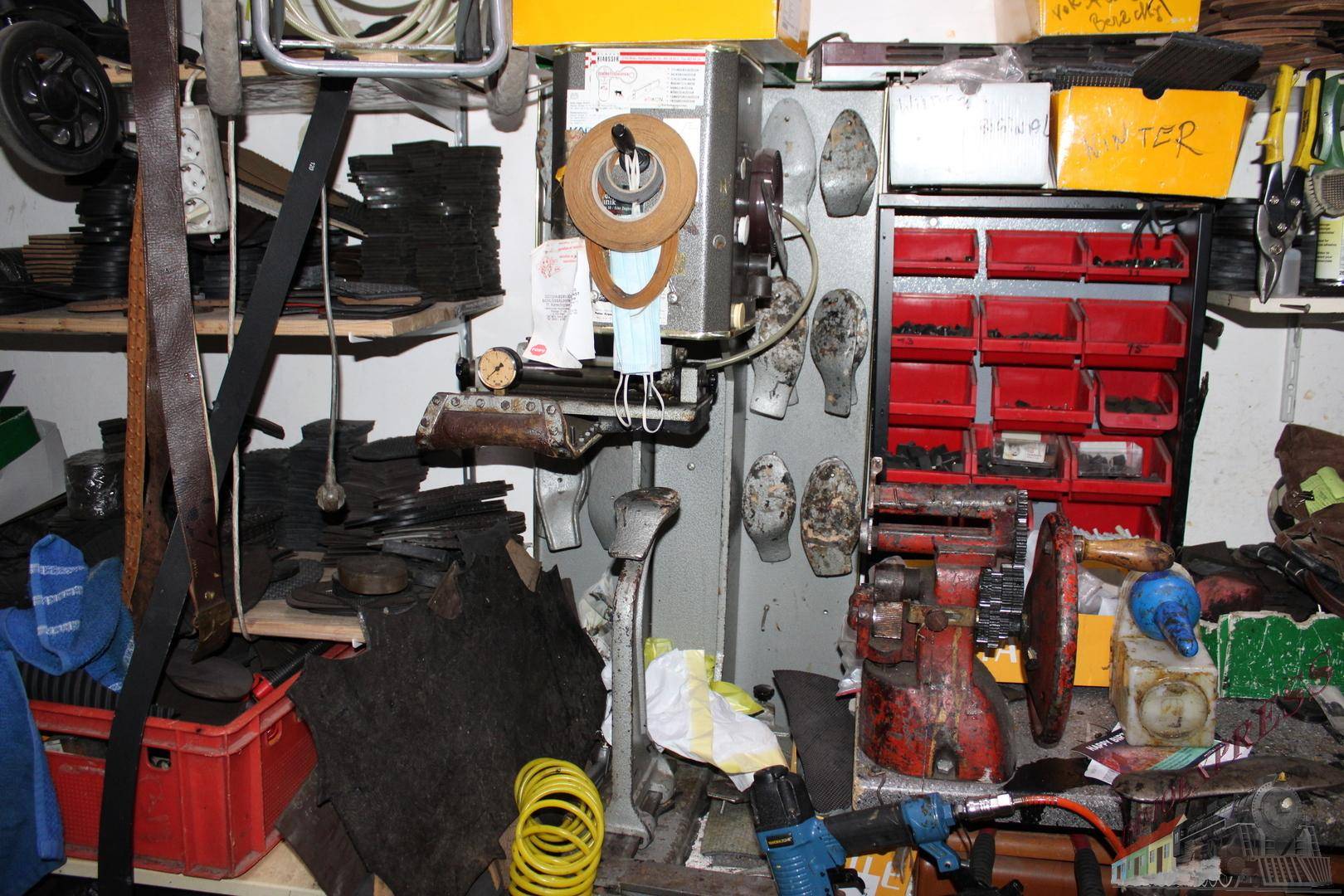 Werkstatt mit verschiedenen Maschinen und Materialien für Schuhreparaturen und Handwerksarbeiten an den Wänden.