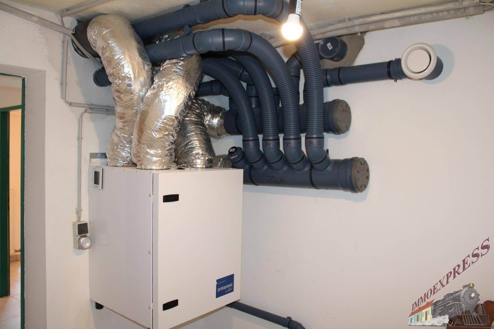 Technikraum mit Lüftungsanlage und sichtbaren Rohren an der Decke.