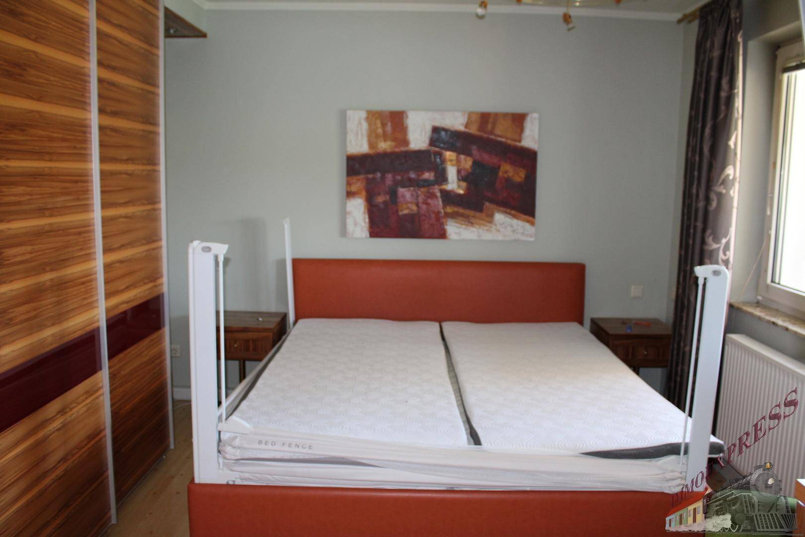 Schlafzimmer mit orangefarbenem Bettrahmen, Holzschrank und Kunstwerk an der Wand.