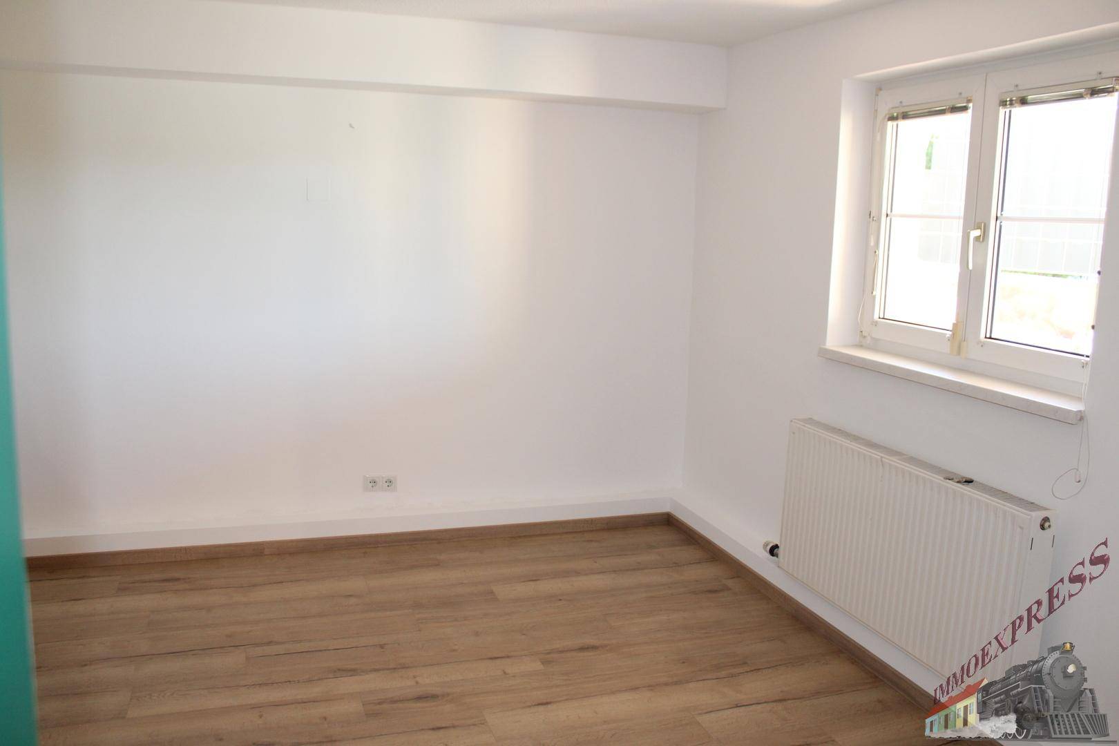 Leerer Raum mit hellem Laminatboden, weißen Wänden und einem Fenster.